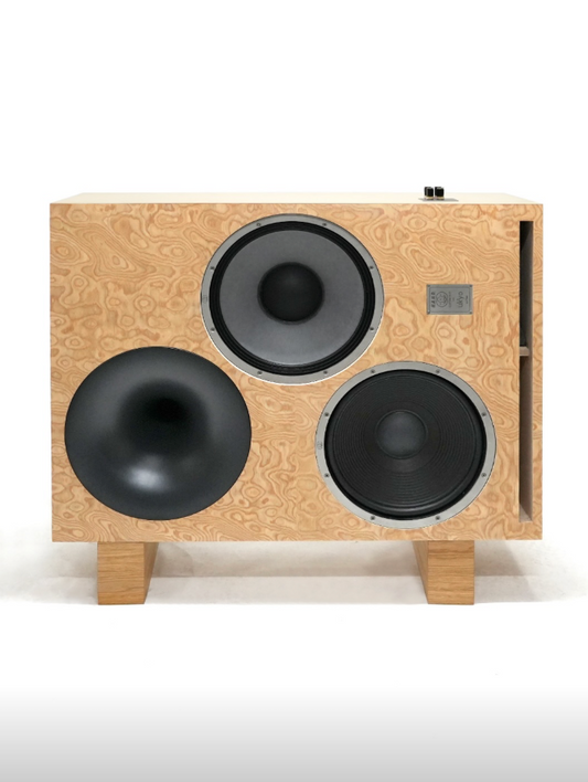 Speaker cabinet with a light natural wood grain front panel, three circular drivers (one large bass driver, two mid-range drivers), and wooden feet, shown against a plain white background.