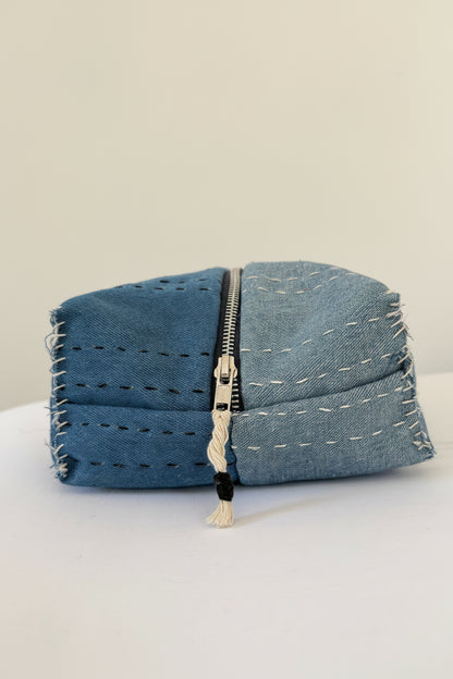 A small zippered pouch made from blue denim fabric, featuring visible stitching and frayed edges.