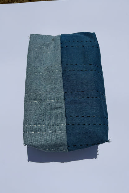 A folded piece of fabric with a vertical split design, featuring a light blue denim-like section on the left and a dark-blue denim-like section on the right, both with sashimi dashed stitching.