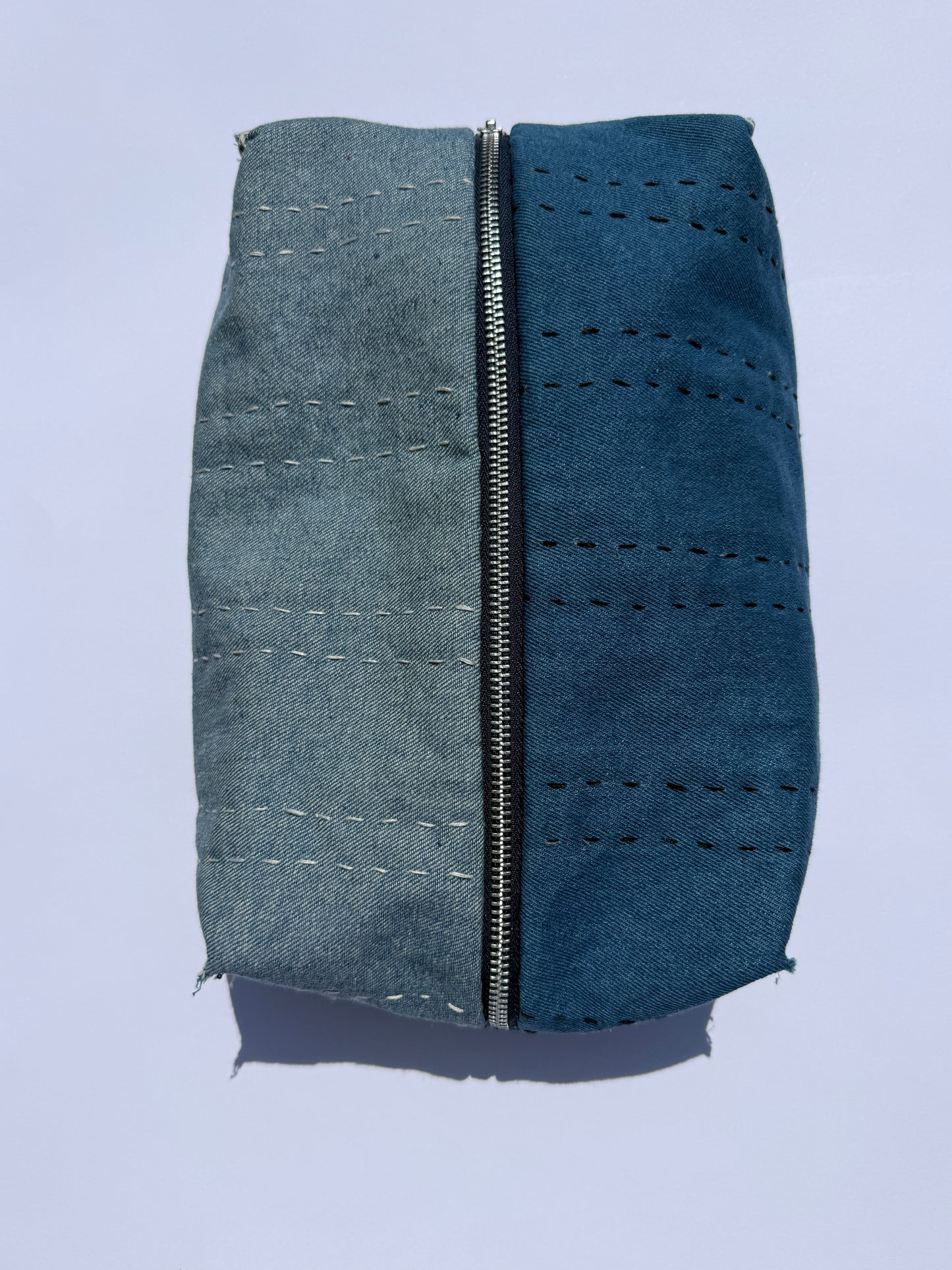 A rectangular zippered pouch or case made from two different colored fabrics side-by-side, featuring a denim-like blue-on the left and a dark-blue on the right, both with stitched details and raw frayed edges.