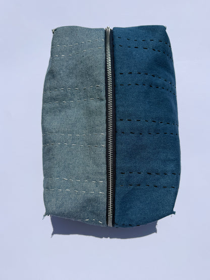 A rectangular zippered pouch or case made from two different colored fabrics side-by-side, featuring a denim-like blue-on the left and a dark-blue on the right, both with stitched details and raw frayed edges.