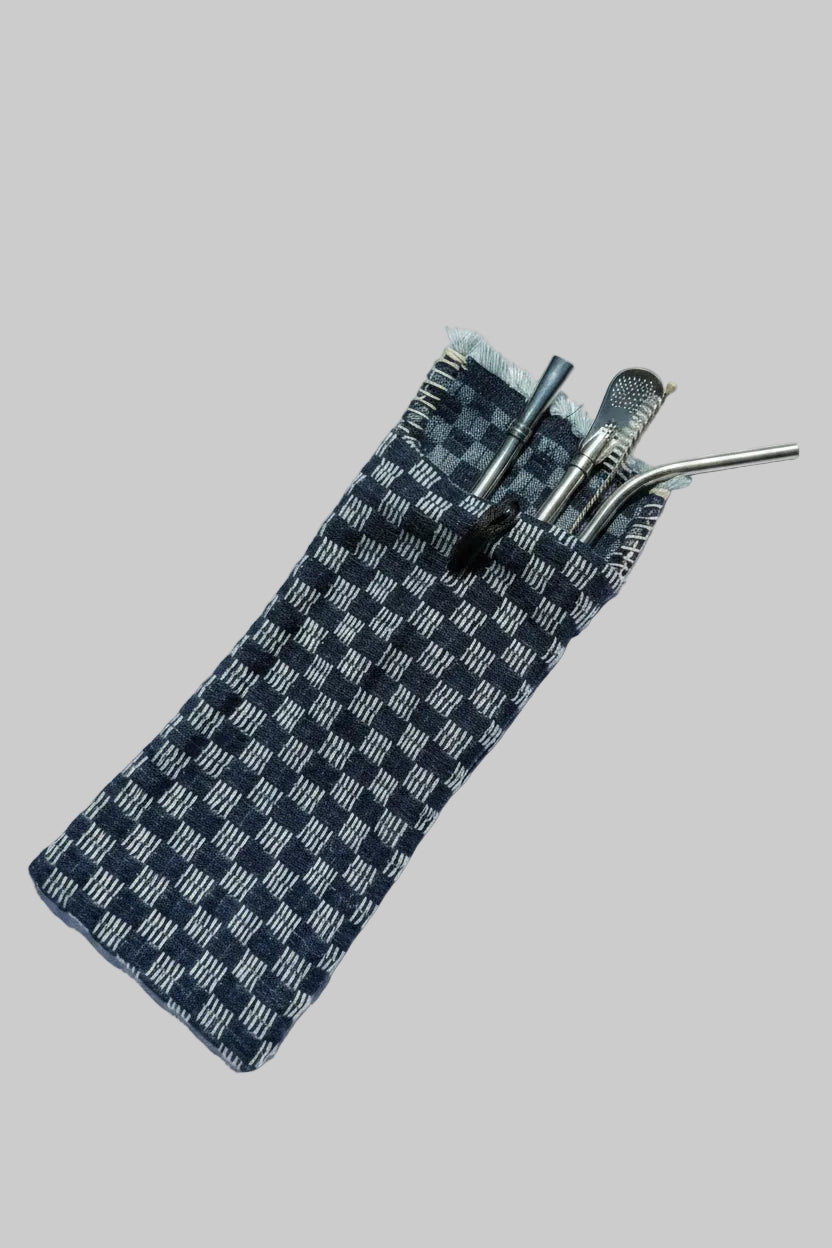 A dark blue and white checkered woven carrying pouch containing three silver metal drinking accessories, including a straw, spoon, and scoop, set against a solid light gray background.